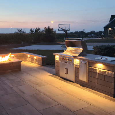 Outdoor kitchen area with grill, drop in cooler, trash, and fire feature.