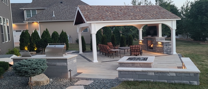 Full view of an outdoor living space with pavilion, outdoor kitchen, fire feature, and landscaping lighting.