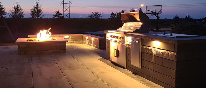Outdoor kitchen with grill, drop in cooler, trash receptacle, and nearby fire feature.